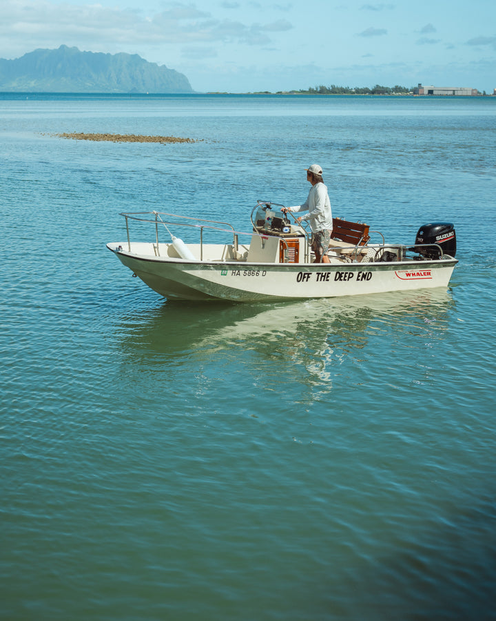 A man in a rashguard and cap pilots a Boston Whaler named &